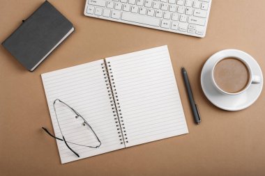 Boş not defteri, klavyesi, bardakları ve kahve fincanı olan bir masa. Üst manzara, düz uzanma.