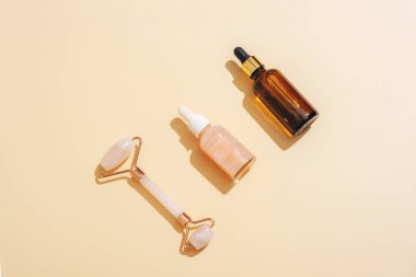 Kozmetik serum şişeleri ve parlak gölgeli bej arka planda yüz silindiri. Cilt bakımı, kaplıca ve sağlık konsepti. Üst manzara, düz uzanma.