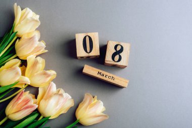 Tahta blok takvimi, 8 Mart tarihi ve gri masada bir sürü sarı lale. Kadınlar günü konsepti. Üst manzara, düz uzanma.