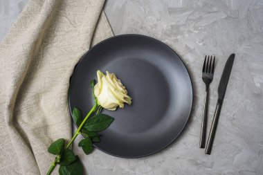 Beyaz gül, siyah tabak ve çatal bıçak takımlı masa takımı. Üst manzara, düz uzanma.