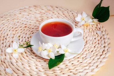 Hasır bir yerde yasemin çiçekli bir fincan yasemin çayı. Üst görünüm.