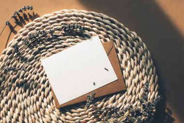 Hasır bir paspasın üzerinde boş bir kartla lavanta çiçekleri olan bir zarf. Üst görünüm, düz görünüm, model.