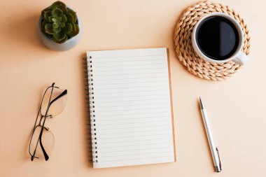 Not defteri, sulu bitki, bardaklar ve kahve, tarafsız bej arka planda. Üst manzara, düz uzanma.