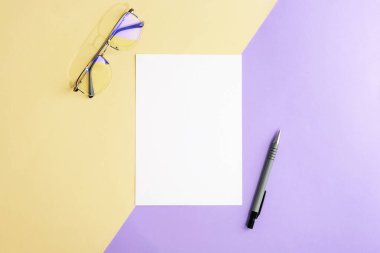 Masaüstü boş kağıt, gözlük ve kalemle bej ve mor iki renkli arka plan. Üst görünüm, düz görünüm, model.
