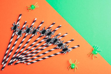 Cadılar Bayramı için örümceklerle pipet içmek turuncu ve yeşil arka planda. Üst manzara, düz uzanma.