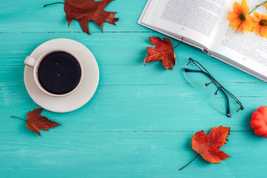 Kahve fincanı, balkabağı, sonbahar yaprakları ve mavi ahşap masa üzerine kitap. Sonbahar, Şükran Günü konsepti. Üst görünüm, düz görünüm, kopyalama alanı.