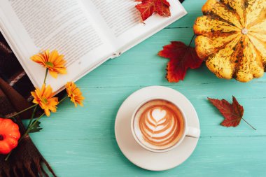 Kahve fincanı, balkabağı, sonbahar yaprakları ve mavi ahşap masa üzerine kitap. Sonbahar, Şükran Günü konsepti. Üst manzara, düz uzanma.