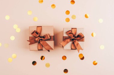 Minimalistic gift boxes with brown ribbons and golden confetti scattered on a beige background for a festive celebration. Top view, flat lay, copy space. clipart