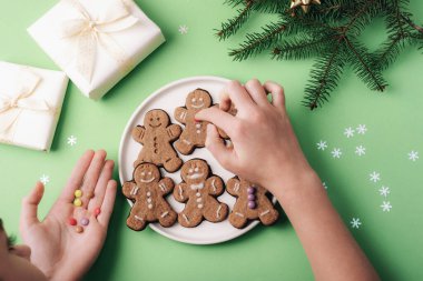 Ellerin zencefilli kurabiyeleri süslü dekorasyonlarla, paketlenmiş hediyelerle ve yeşil arka planda çam dallarıyla süslemesinin en üst görüntüsü..