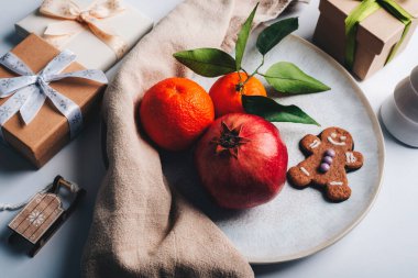 Nar, portakal, zencefilli kurabiye ve beyaz bir tabakta paketlenmiş hediyelerle şenlikli bir hayat. Noel konsepti. Üst görünüm.