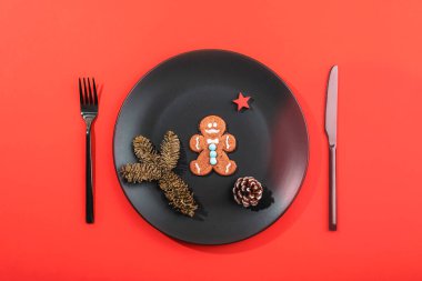 Siyah bir tabakta zencefilli kurabiye. Kırmızı arka planı ve dekorasyonu çok az. Üst manzara, düz uzanma.