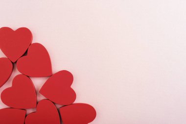 Kırmızı ahşap kalpler yumuşak pastel pembe arka planda dizilmiş. Sevgililer Günü konsepti. Üst görünüm, düz görünüm, kopyalama alanı.