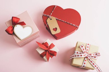 Kırmızı kurdeleli çeşitli hediye kutuları ve yumuşak pembe arka planda düzenlenmiş kalp süslemeleri. Sevgililer Günü konsepti. Üst manzara, düz uzanma.