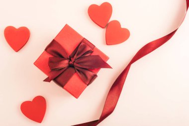 Kırmızı hediye kutusu, kurdeleli ve hafif arka planlı kalpler. Sevgililer Günü konsepti. Üst görünüm, düz görünüm, kopyalama alanı.