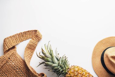 Düz bir torba, olgun bir ananas ve beyaz bir arka planda hasır bir şapkayla yatıyordu. Üst görünüm, düz görünüm, kopyalama alanı.