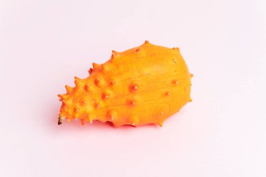 Yumuşak pembe arka planda dikenli turuncu derili canlı boynuzlu kavun. Kiwano meyvesi, yakın plan..
