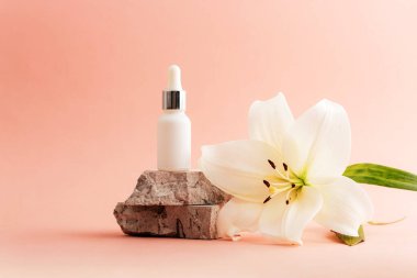 Beyaz kozmetik serum düşürücü şişesi üzerinde pembe arka planda beyaz bir zambak çiçeği var. Doğal kozmetik konsepti. Yakın çekim..