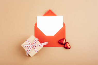 Kırmızı zarf ve bej arka planda kalp şeklinde süslemeleri olan küçük hediye kutusu aşkı simgeliyor. Sevgililer Günü konsepti. Üst görünüm, düz görünüm, model.