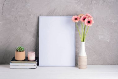 İçinde pembe Gerbera çiçekleri olan boş bir çerçeve ve arka planda gri dokulu duvarlar olan kitaplar. Model.