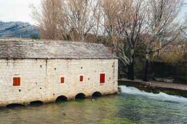 Ağaçlarla çevrili bir nehir kıyısında kırmızı panjurlu eski taş su değirmeni. Hırvatistan 'ın Solin kentindeki Jadro nehrinde Gaspina mlinica adlı geleneksel 17. yüzyıl su değirmeni.