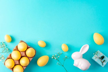 Sarı Paskalya yumurtaları, beyaz tavşan, hediye kutusu ve mavi arka planda çiçekler. Üst görünüm, düz görünüm, kopyalama alanı.