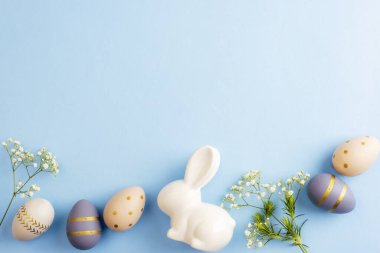 Mavi arka planda Paskalya yumurtaları, çiçekler ve seramik tavşanlar. Paskalya konsepti. Üst görünüm, düz görünüm, kopyalama alanı.