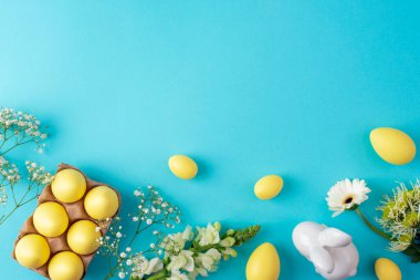 Sarı paskalya yumurtaları ve beyaz bahar çiçekleri mavi arka planda seramik tavşanlı. Üst görünüm, düz görünüm, kopyalama alanı.