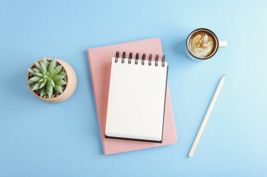 Not defteri, kahve fincanı, kurşun kalem ve mavi pastel arka planda sulu çalışma alanı. Üst görünüm, model.