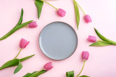 Pembe laleler pembe arka plandaki boş gri tabağın etrafına dizilmiş. Üst görünüm, düz görünüm, model.