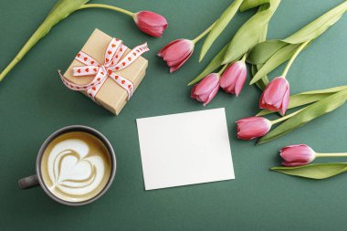 Kahve, hediye kutusu, laleler ve koyu yeşil arka planda boş kart. Tatil konsepti. Üst görünüm, düz görünüm, model.