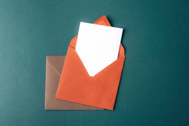 Koyu yeşil zemin üzerinde beyaz kart olan turuncu ve kahverengi zarflar. Üst görünüm, düz görünüm, model.