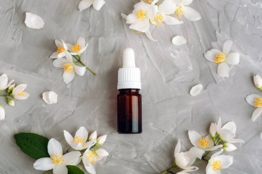 Kozmetik esaslı yağ şişesi ve gri desenli arka planda beyaz yasemin çiçekleri. Doğal kozmetik, cilt bakımı konsepti. Üst manzara, düz uzanma.