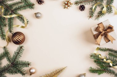 Yeşil çam dallı Noel kompozisyonu, bej arkaplanda sıralanmış kurdeleli bronz hediye kutuları ve süslemeler. Üst görünüm, düz görünüm, kopyalama alanı.