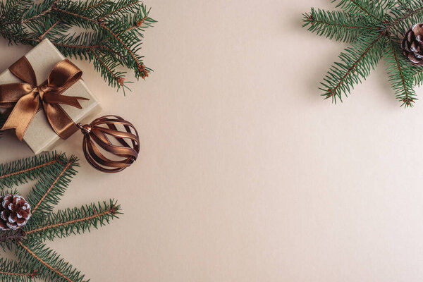 Рождественская квартира лежала с зелеными сосновыми ветвями, бронзовая подарочная коробка с ленточкой и украшениями на бежевом фоне. Вид сверху, пространство для копирования.