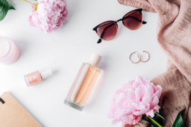 Kadınların bembeyaz arka planında pembe şakayık çiçekleri olan düz kozmetik ürünleri ve şık aksesuarları vardı. Güzellik, moda konsepti. Üst manzara, düz uzanma.