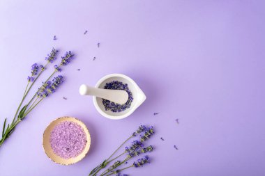Havan topu ve lavanta çiçekli kabuk ve mor arka planda bir kasede banyo tuzu. Doğal şifalı bitkiler ilaç konsepti. Üst manzara, düz uzanma.