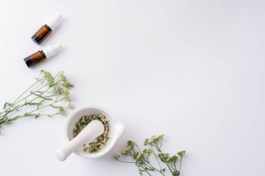 Havan topu ve kabuklu kuru otlar ve beyaz arka planda gerekli yağ şişeleri ve kiremit çiçekleri. Üst görünüm, düz görünüm, kopyalama alanı.
