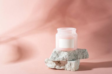 Taş podyumun üstündeki boş etiketli kozmetik kavanozu. Işıklı ve gölgeli pembe arka plan. Model.