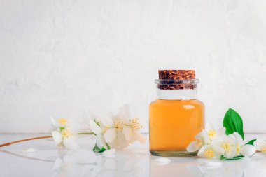 Mantar kapaklı cam yağ şişesi ve beyaz arka planda yasemin çiçekleri. Boşluğu kopyala.