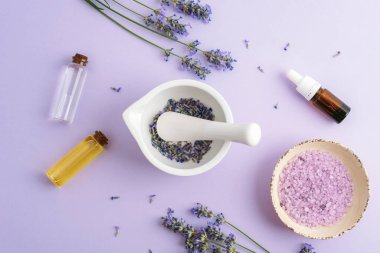 Kâsede lavanta banyosu tuzu, lavanta çiçekli harç ve kabuk mor arka planda aroma esansı. Doğal bitkiler ilaç, aromaterapi konsepti. Üst manzara, düz uzanma.