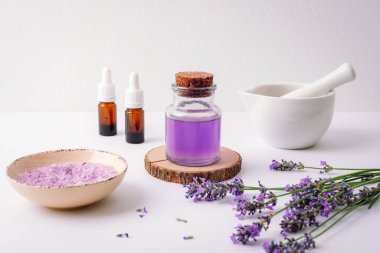Cam şişe lavanta yağı, deniz tuzu, havan topları ve beyaz arka planda taze lavanta çiçekleri. Aromaterapi kavramı.