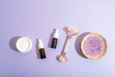 Krema kavanozlu spa seti, gerekli yağ şişeleri, yüz silindiri ve leylak arkaplanlı deniz tuzu. Üst görünüm, alanı kopyala.