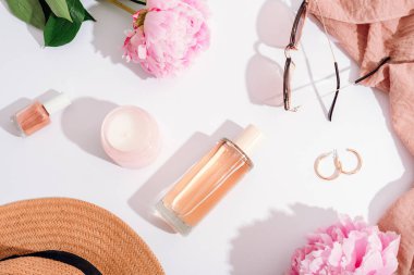 Kadınların düz yatakları kozmetik ürünler, şık aksesuarlar, beyaz arka planda pembe şakayık çiçekleri ve keskin gölgeler. Güzellik, moda konsepti. Üst görünüm.