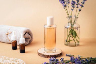 Parfümlü cam kozmetik şişesi, gerekli yağlar, havlu ve bej arka planda taze lavanta çiçekleri. Aromaterapi kavramı.