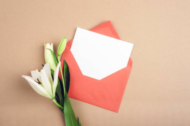 Beyaz açık kart, kırmızı zarf içinde bej arka planda beyaz zambak çiçekleri. Üst görünüm, düz görünüm, model.