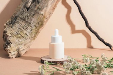 Ahşap tezgahta serum şişesi ve tarafsız bej arka planda parlak gölgeli korkuluk çiçekleri. Doğal kozmetik, cilt bakımı. Yakın çekim..