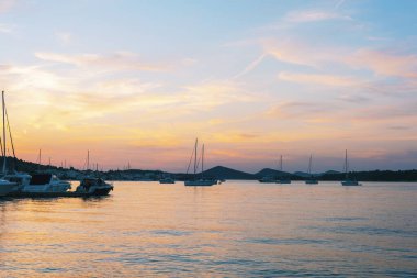 Gün batımında yelkenliler ve yatlar sakin denizde, renkli gökyüzüyle. Hırvatistan 'ın Cinayet Adası.