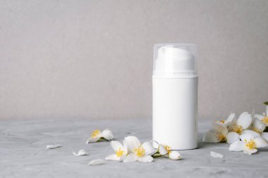 Beyaz kozmetik şişesi ve gri arka planda yasemin çiçekleri. Doğal kozmetik, spa ve sağlık konsepti. Boşluğu kopyala.
