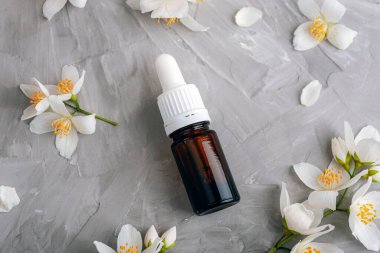 Kozmetik yağı ve beyaz yasemin çiçeğiyle dolu bir şişe. Doğal kozmetik, cilt bakımı konsepti. Üst manzara, düz uzanma.