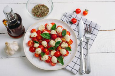 Çeri domatesli İtalyan caprese salatası, mozzarella, fesleğen, beyaz ahşap masada balzamik sos. Üst manzara, düz uzanma.